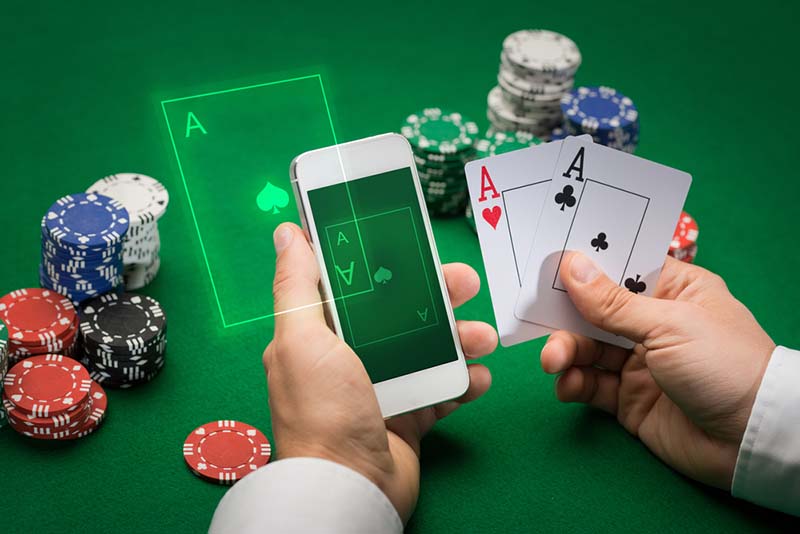 kockarnica, online kockanje, krupni plan igrača pokera s igraćim kartama, pametnim telefonom i žetonima za zelenim stolom kasina